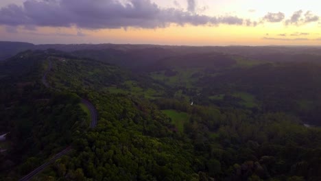 aerial view of hills and road in a tropical forest valley at sunset