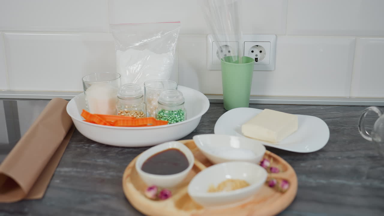 소스, 설탕 및 향신료로 가득 찬 세라 그, 접시에 버터, 유리 항아리, 쿠키 커터 및 전원 소켓에 베이킹 재료를 담은 나무 트레이가 있는 현대 주방 카운터