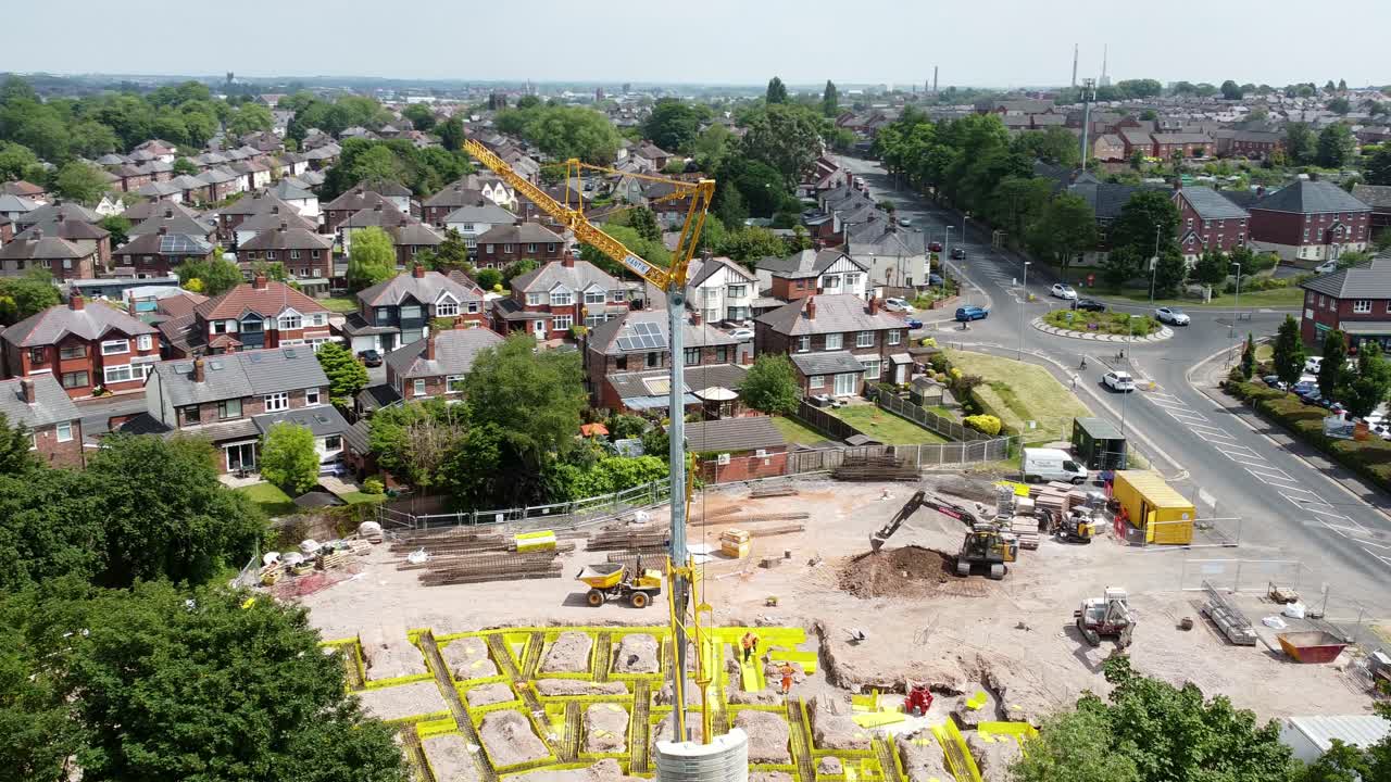 Tall crane setting building foundation in British town neighbourhood aerial view above townhouse rooftops