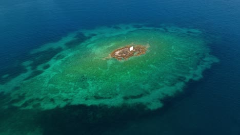 topdown aerial establishing of small circular reef or islet in deep blue greek waters