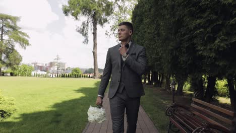 Groom-goes-down-the-alley-between-bushes-with-a-wedding-bouquet-to-his-beloved-bride,-first-meeting