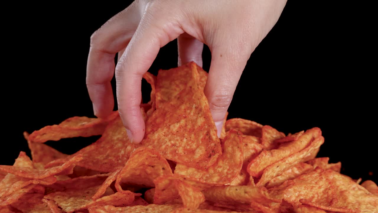 Ludzka ręka wybiera i podnosi tortilla chip z apetycznego stosu nachos, oświetlenie studyjne, statyczna kamera