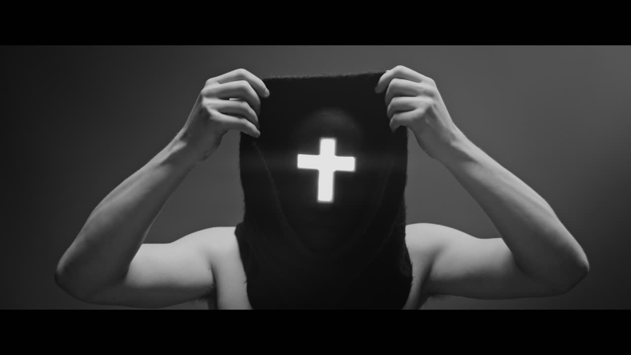 Masked man with cross of light glowing on his face puts on a hood