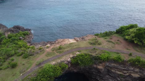 broken beach of nusa penida with a footpath on natural arch bridge covered in lush green vegetation