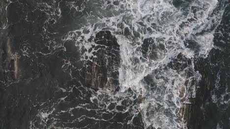 two waves crashing over two exposed rocks at sunrise aerial top down