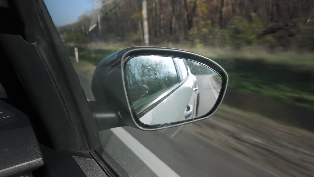 Viaggio in auto attraverso la campagna rumena riflessa nello specchietto retrovisore di un'auto in movimento