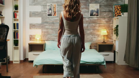 hermosa mujer rubia en pijama cayendo de nuevo en su cama