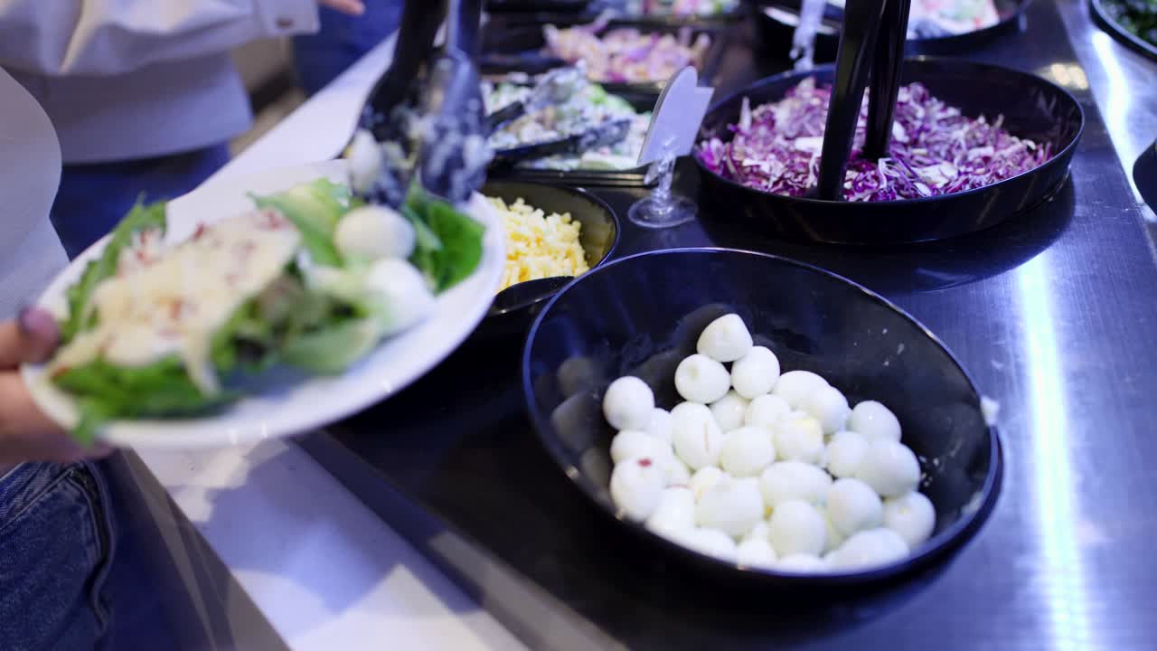 Primo piano di una donna che aggiunge uova di quaglia a un piatto di insalata fresca al buffet