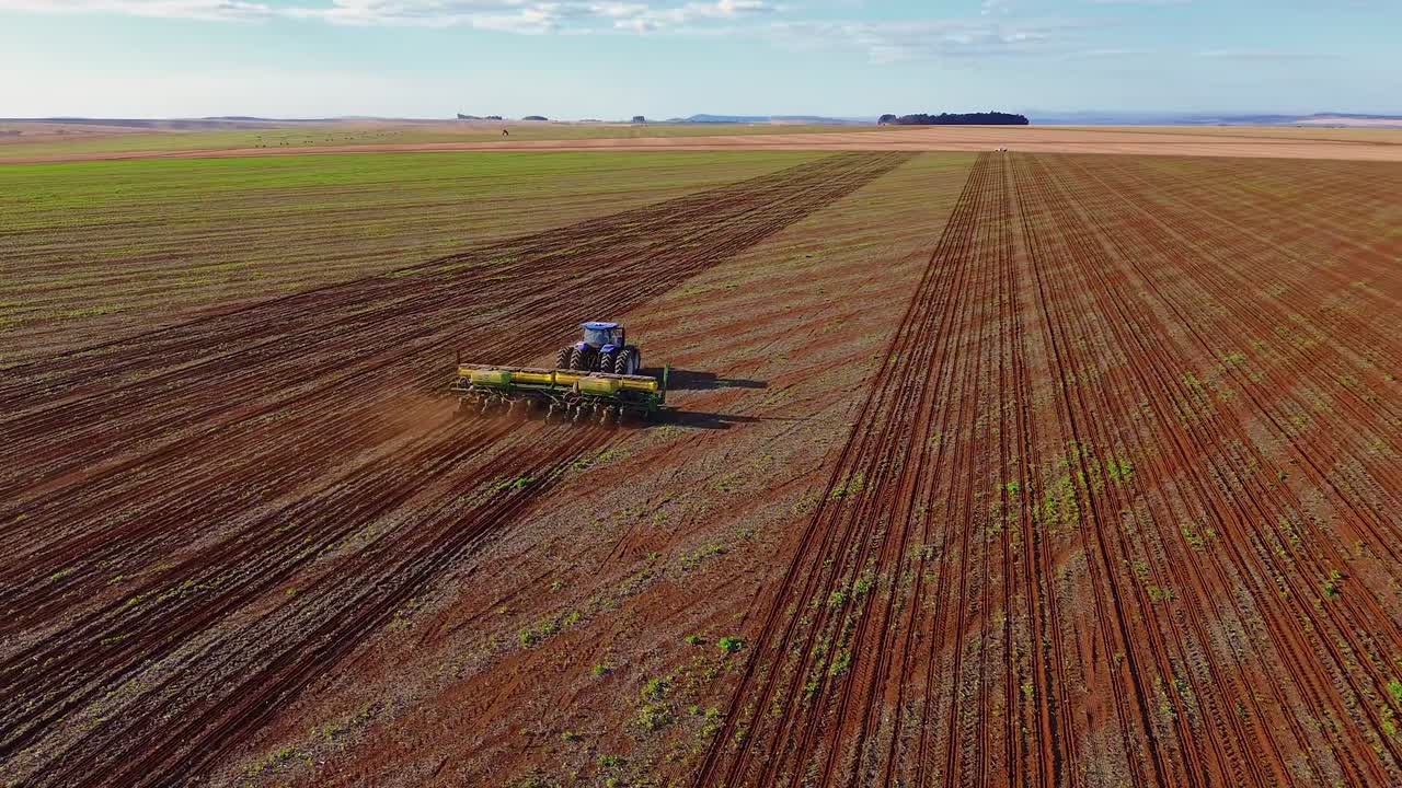 La semina della soia avanza con un trattore che traina una seminatrice per colture a file larghe dotata di dosatori di semi, serbatoi per fertilizzanti e guida automatica GPS attraverso file di terreno strutturate a Formosa, Goias, Brasile, ripresa aerea.