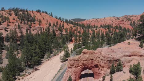 aerial footage over a road, red rock and a tunnel with cars passing through