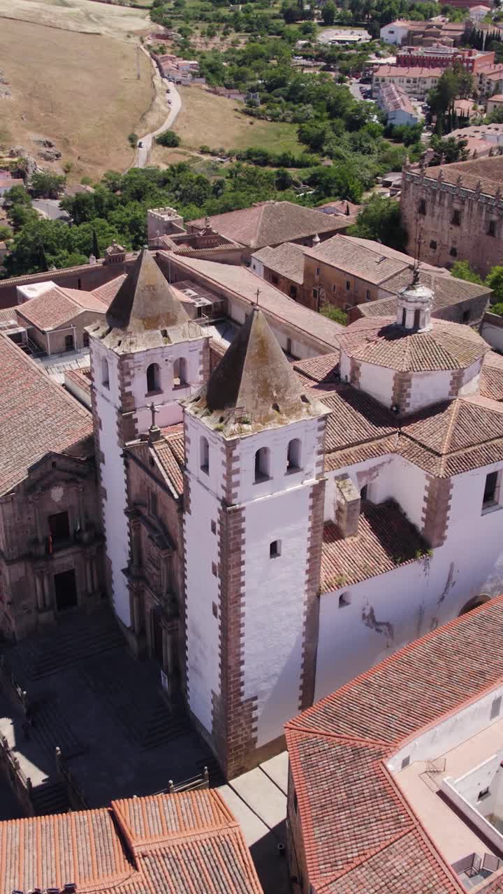 Blanca medieval Iglesia de San Francisco Javier en Cáceres, España. Vista aérea vertical que destaca su arquitectura histórica y el paisaje urbano circundante.