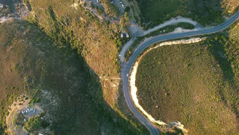 Vista-Aérea-De-Arriba-Hacia-Abajo-Del-Coche-Dando-La-Vuelta-A-Una-Curva-De-Montaña-Al-Atardecer,-Pico-De-Chapmans