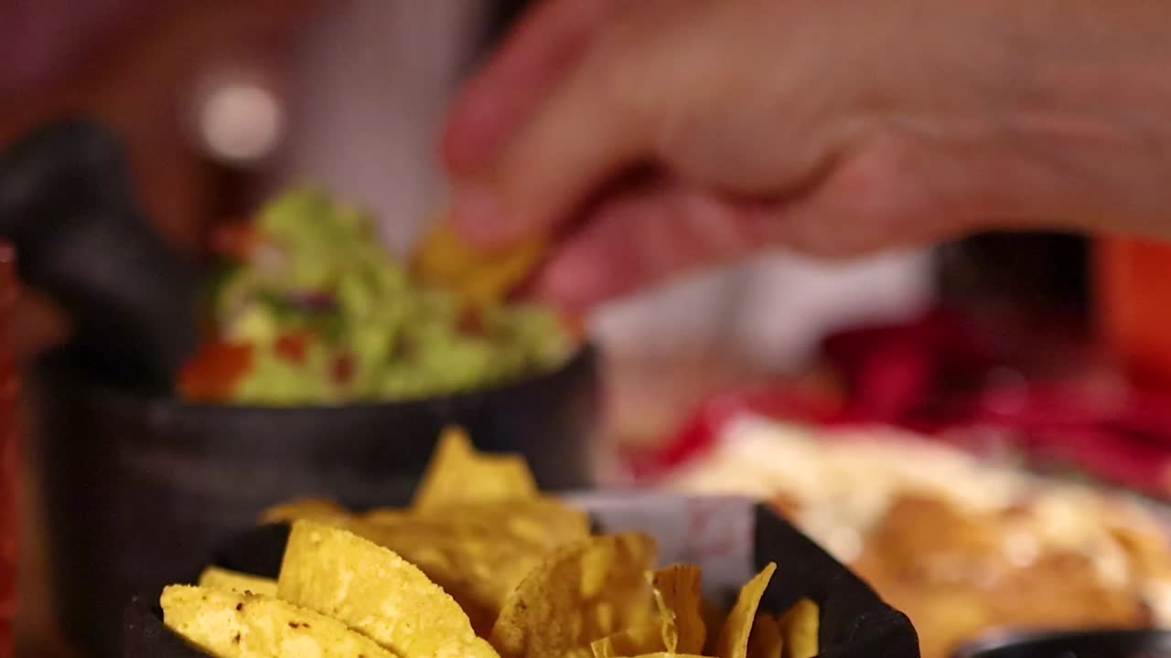 Primo piano di una mano che intinge una croccante patatina nacho in una ciotola di guacamole fresco.