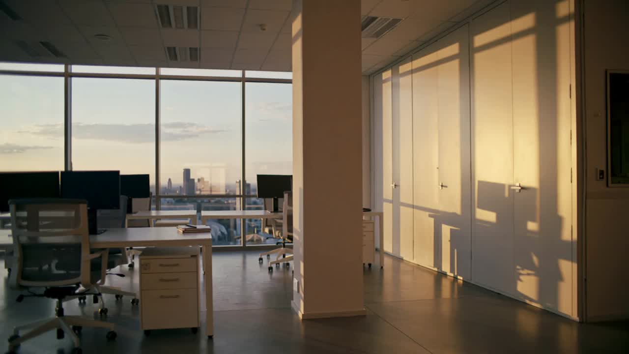 Pushing camera recording open-plan high-rise office, sun shifting shadows across desks showing time