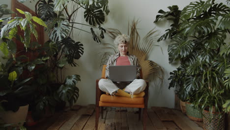 mujer joven trabajando en una computadora portátil en una habitación con plantas