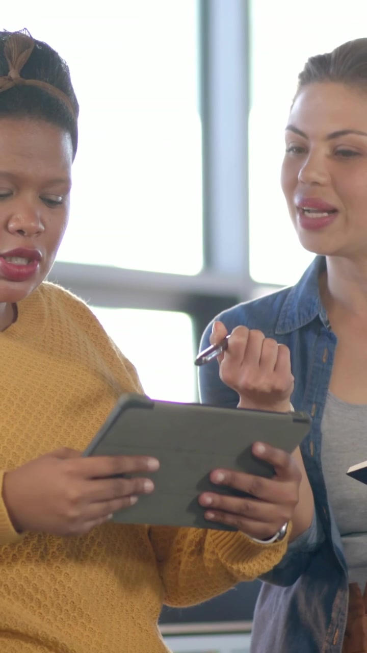 Vertikal video: Åbner notesbog, par i denim læner sig mod tablet på kontor, peger med pen og gennemgår.