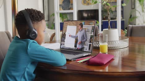 african american boy using laptop for video call, with male teacher on screen