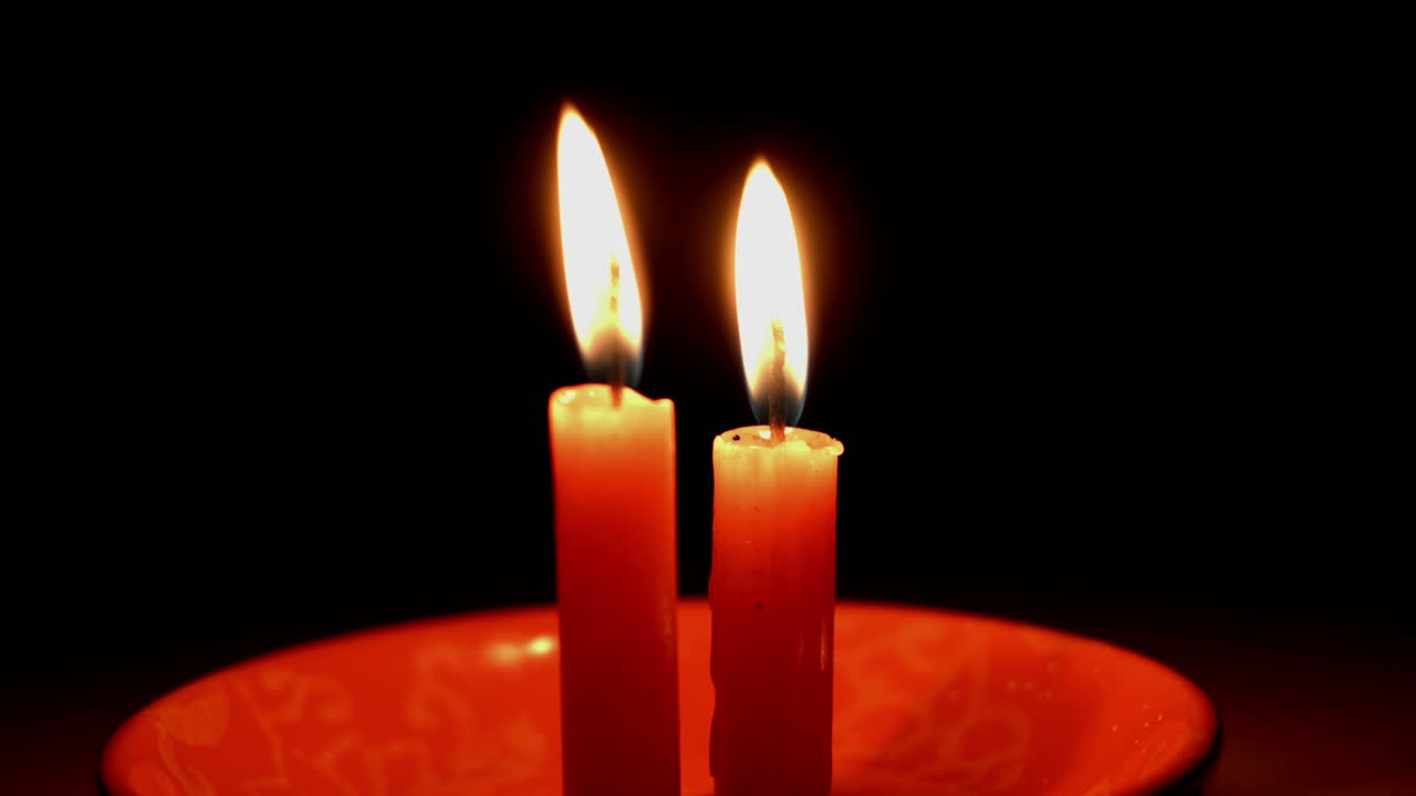Primo piano di una mano che accende due candele rosse al buio