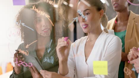 Diverse-businesswomen-writing-on-glass-wall-and-brainstorming-at-office,-in-slow-motion