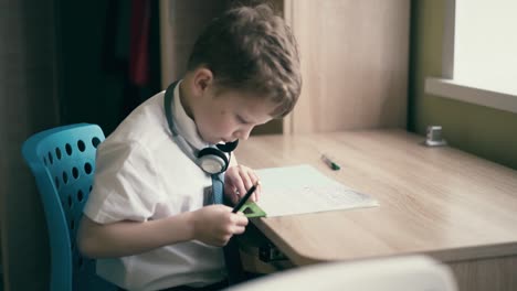 niño de escuela hace la tarea se sienta en auriculares dibuja en un cuaderno con una vara de medida triangular