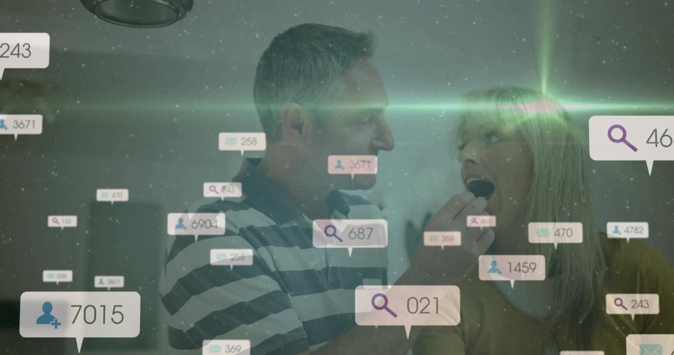 Mature man feeding woman snack in home kitchen while data bubbles rising showing marketing boost