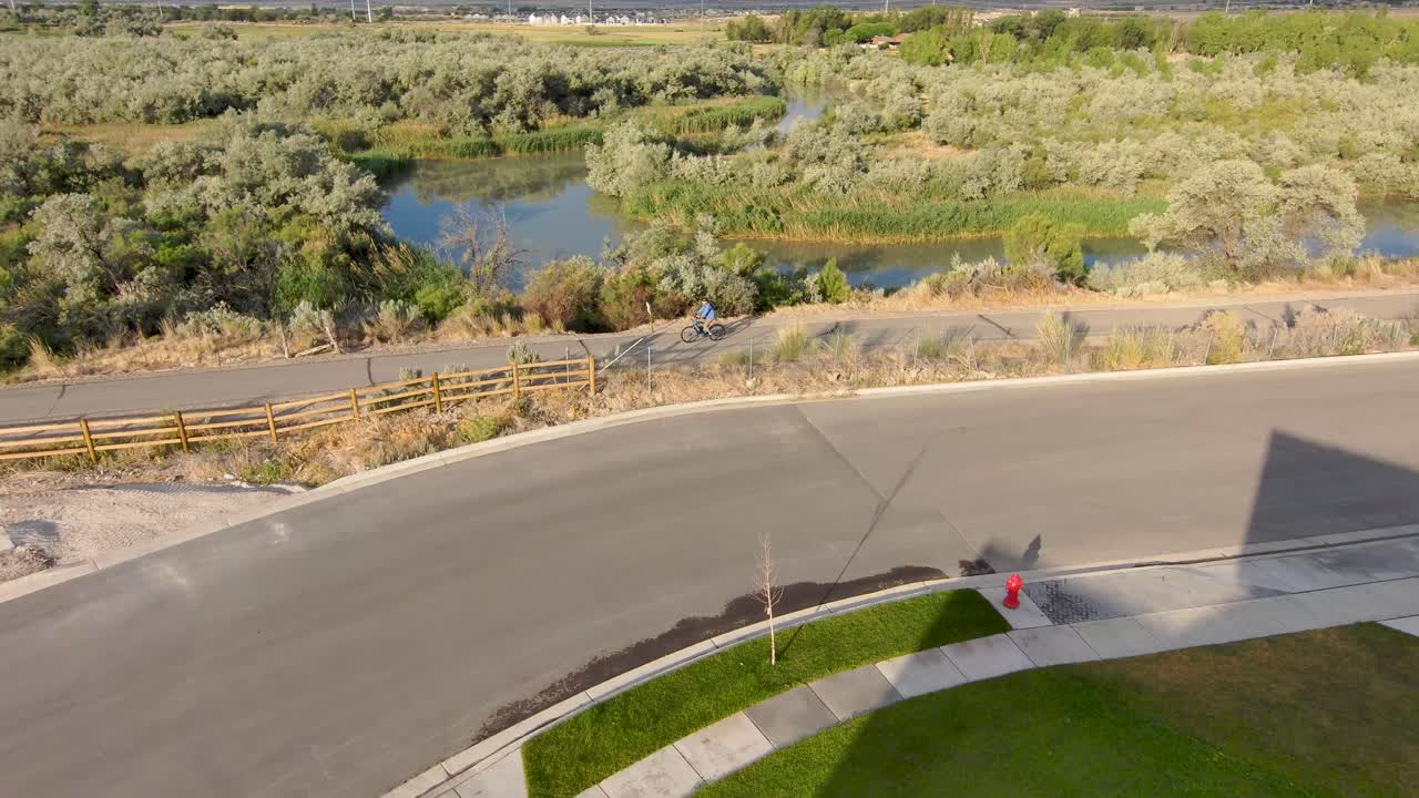 하늘이 물 표면에 반사되는 강 옆 길을 따라 자전거를 타는 남자 - 공중 전망