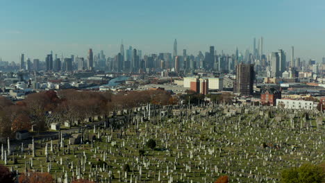 Forwards-fly-above-historic-Calvary-Cemetery-with-tall-modern-high-rise-buildings-in-background.-Queens,-New-York-City,-USA