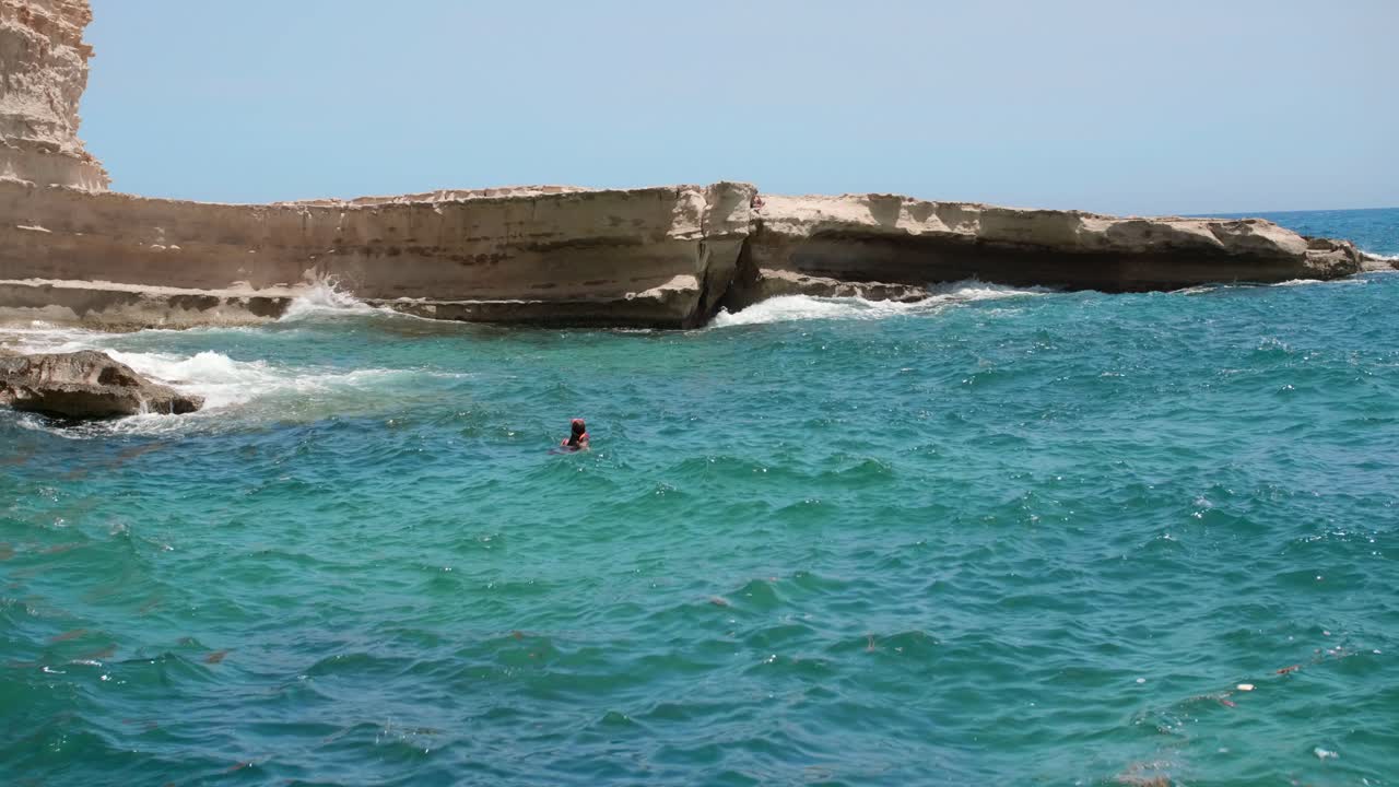 buceador solitario en el mar mediterráneo junto a la pintoresca costa rocosa de la isla de malta, amplia vista