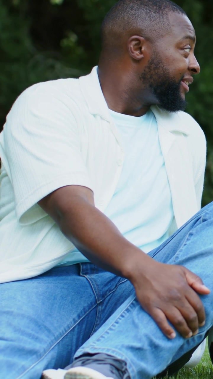 Vertical video: Turning man in blue tee and jeans reacting to off-frame voice at park eyeing ball
