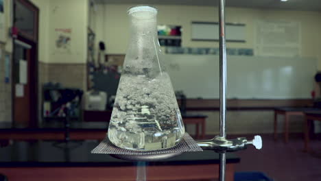 agua hirviendo en un matraz erlenmeyer, calentado por mechero bunsen en un aula de química