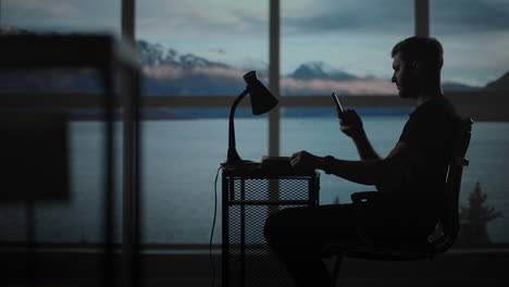 silhouette of a man sitting at a table looking at a mobile phone thinking and analyzing the stock market solving personal problems repayment of loans internet banking