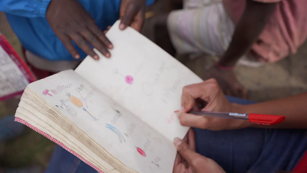 Caucasian white volunteer reviewing African children's homework at school with lack of resources