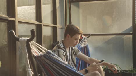 Man-Resting-In-A-Hammock-And-Using-His-Mobile-Phone---close-up