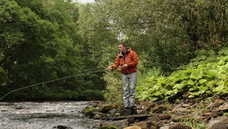 Hand-held-shot-of-a-flyfisherman-walking-along-a-rocky-riverbank-and-casting