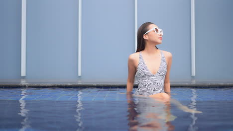 a young woman in a zebra print bathing suit refreshes in the shallow water of a resort pool