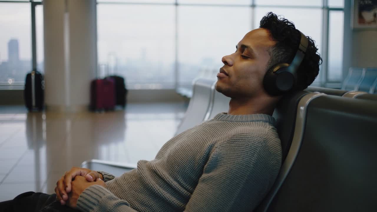 Resting traveler awaiting flight wearing gray sweater, headset in airport, suitcase, copy space