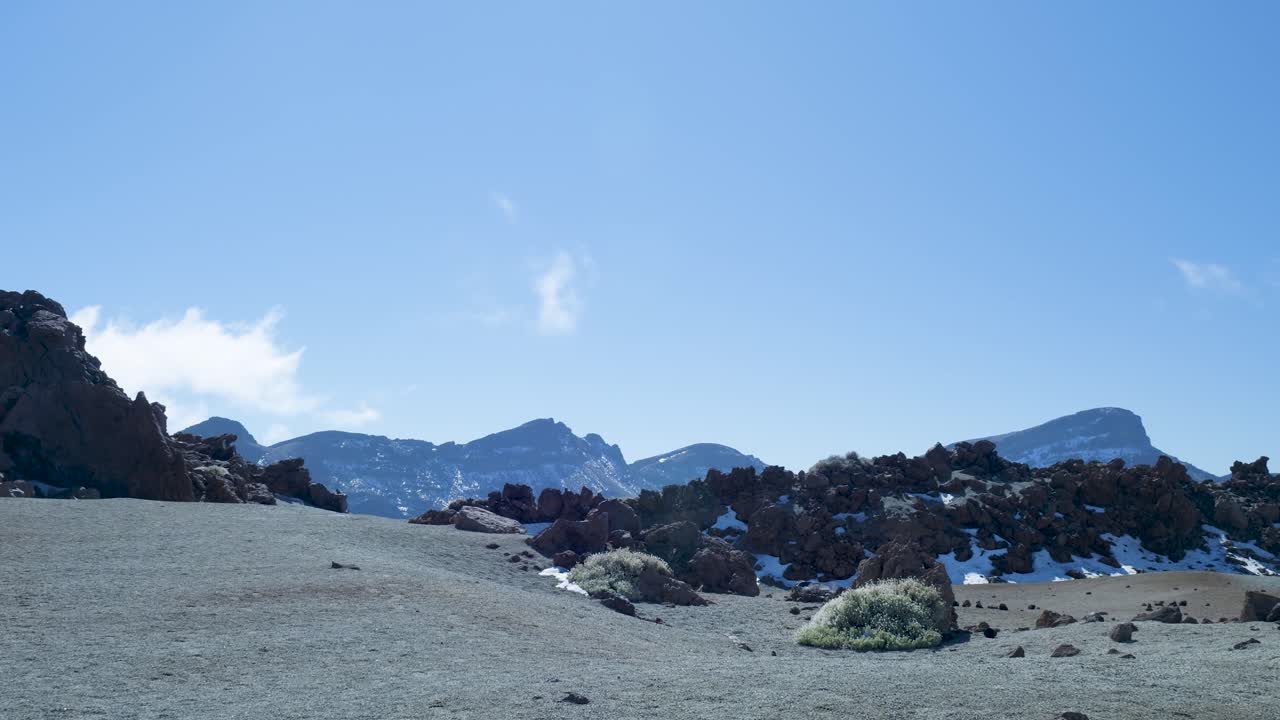 Paesaggio vulcanico arido con montagne innevate in lontananza