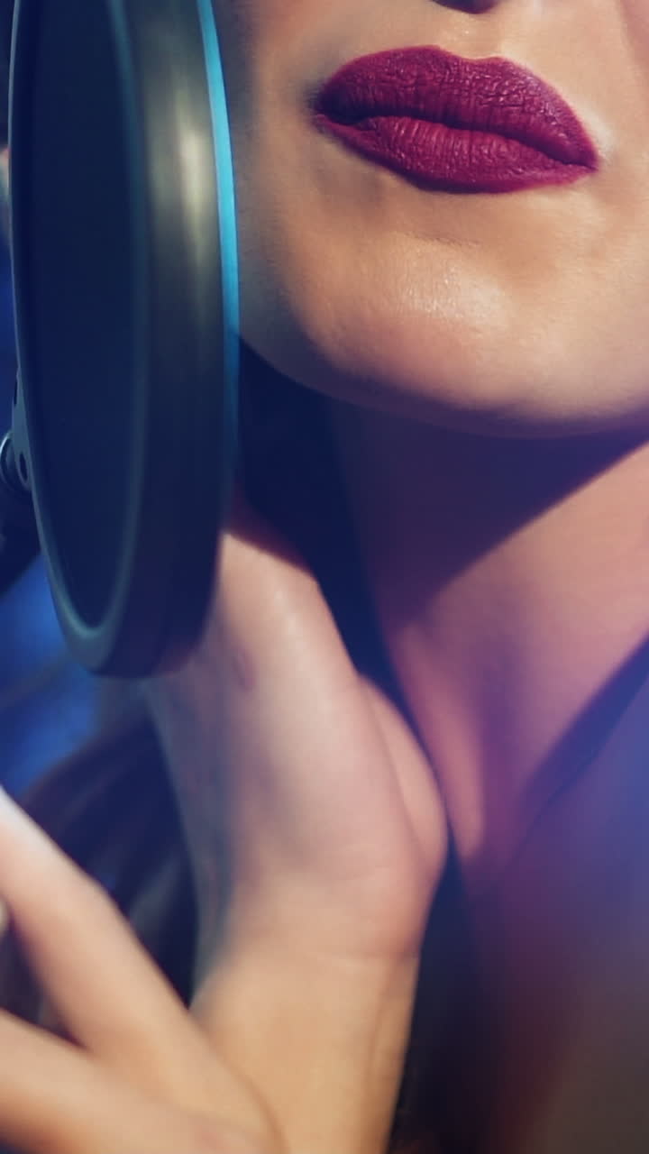 pretty woman with bright lipstick is holding a microphone in her hand and singing in headphones in an audio studio. Close-up Vertical video