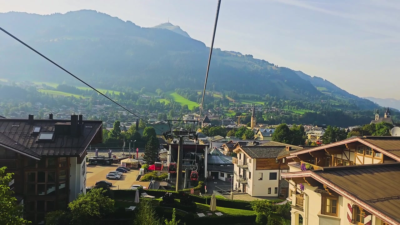 Panorama alpino con cavi della funivia, tetti di villaggi turistici, campanili di chiese, valli verdi e montagne che brillano nella morbida luce del sole mattutino durante un tranquillo viaggio estivo in Europa