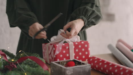 close-up of a woman decorator with scissors cuts and trims the ribbon on the packaging of a gift for christmas