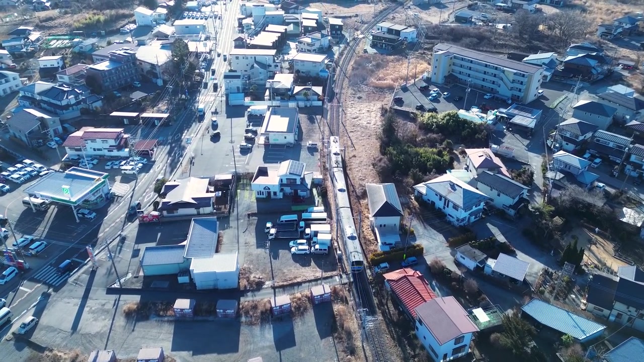 日本、河口湖町の市街地や村の住宅地を通り抜け、鉄道の線路を走る列車と、近くの道路を走る車を捉えたドローン空撮風景。アジアの交通と旅行の情景。