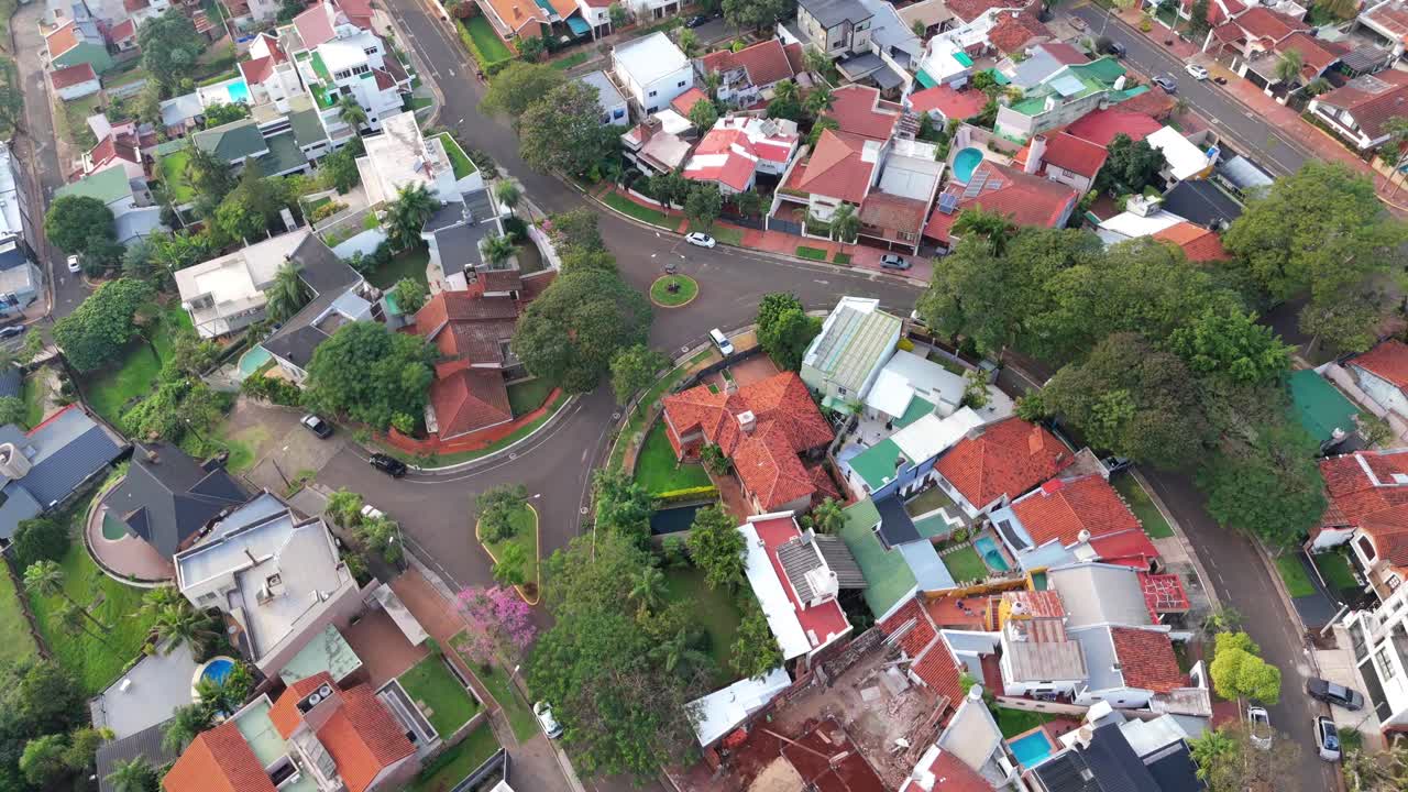 A high-angle aerial drone shot of an upscale residential neighborhood in Posadas, Misiones, Argentina. The view shows a roundabout and dense housing with red tile roofs