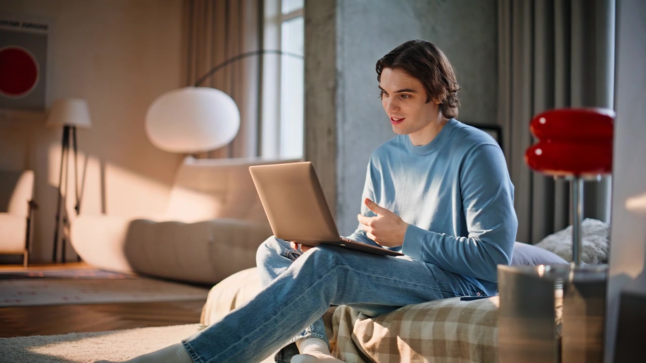 Giovane uomo d'affari che usa il laptop seduto a letto la mattina presto. Uomo in videochiamata.