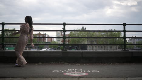 fashionable latina tourist with black wavy hair and a floral dress walking and spinning in london with a view of boats and buildings behind her