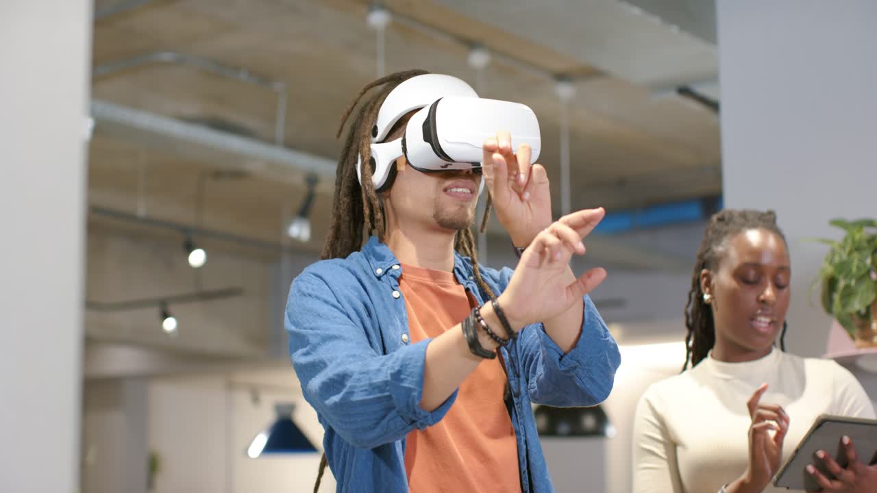 Personale afroamericano che testa la VR in ufficio, l'utente con il visore usa i controlli mentre un collega è al tablet.