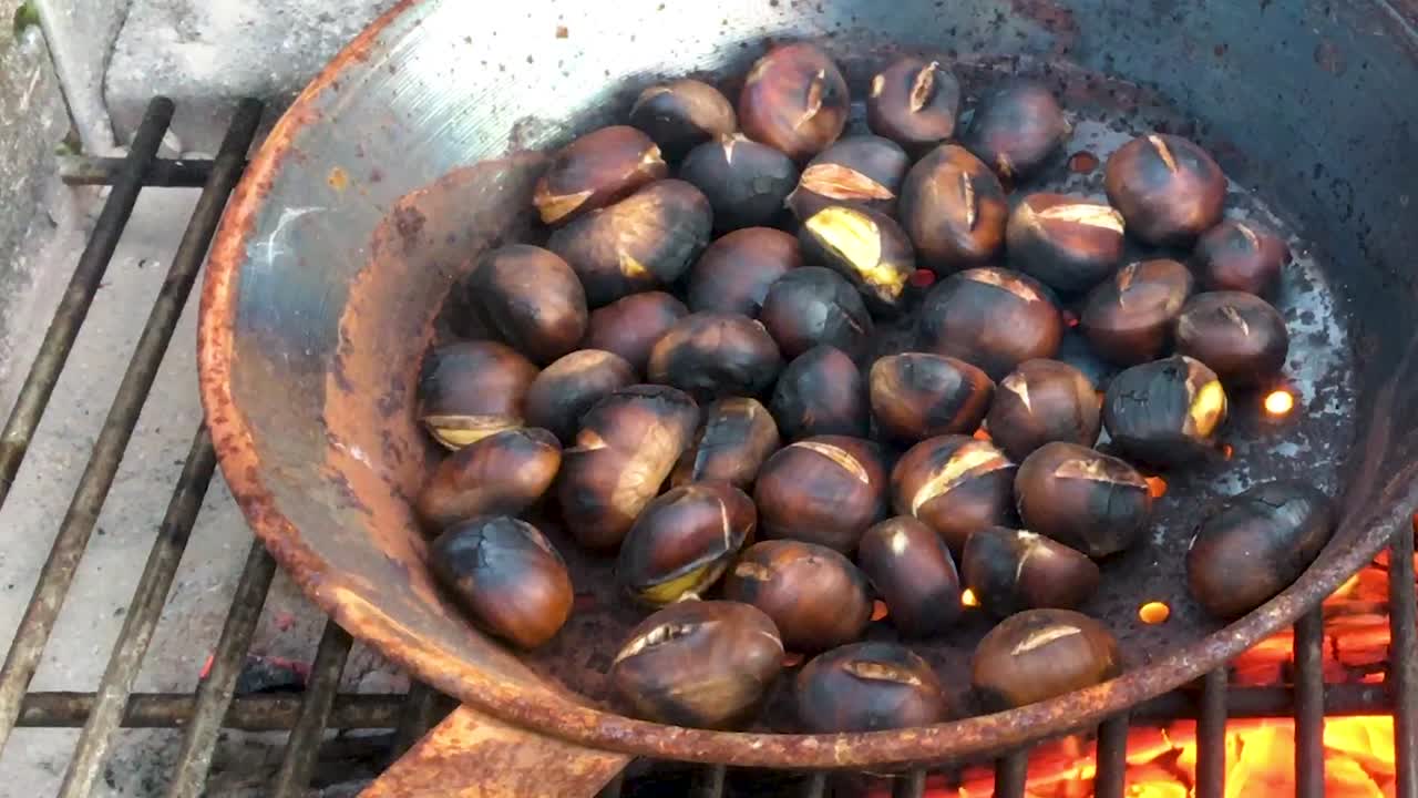 Chestnuts roasted on open fire, seasonal delicacy, harvest, 1920 HD, holiday favorite food, close up, roasting in iron pan, crane shot low to high revealing chestnuts