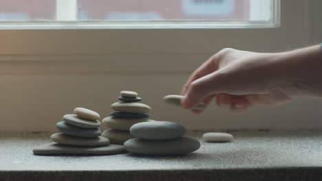 Female-hands-stacking-pebbles-on-windowsill-in-apartment,-indoors-decoration