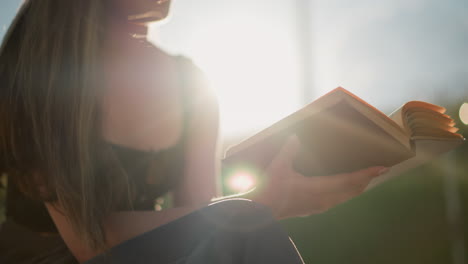 sunlight reflects off pages of book held by woman in black signet seated outdoors, as wind gently blows through the open pages. background is softly blurred