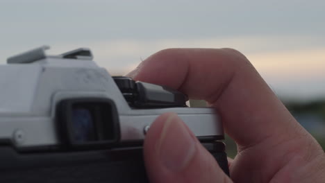 Close-up of a Person's Hand Holding and Operating a Vintage Film Camera at Sunset