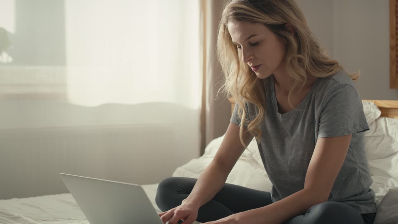 Caucasian woman sitting on the bed and using the laptop at morning